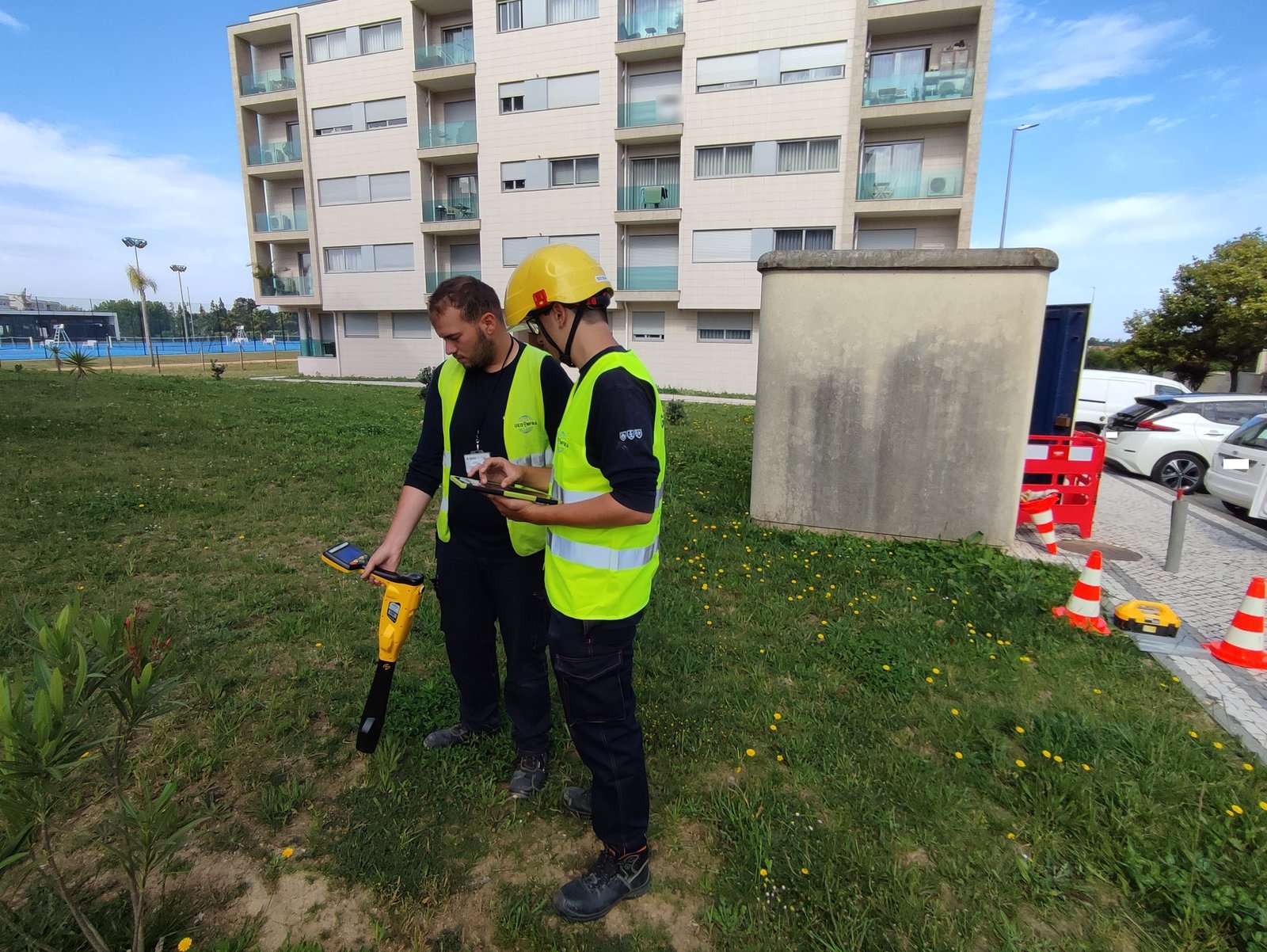 Dois técnicos da Geoinfra no terreno, junto a um armário da rede, com um localizador de cabos e um tablet de recolha de dados